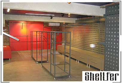 Часть выставочного зала магазина спортивных товаров, где присутствуют вешала для одежды и много функциональные пристенные решетки. 
